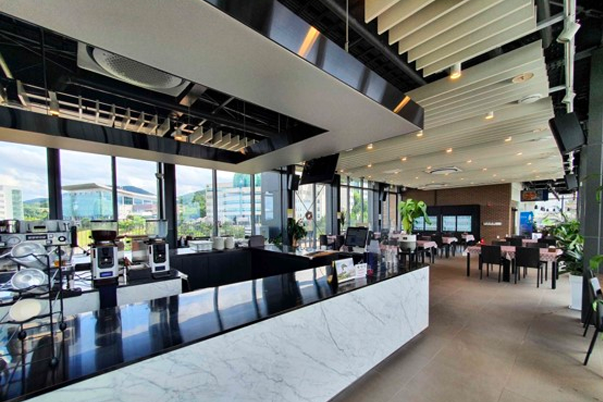 大邱韩医大学食堂内部现代化设计，宽敞的用餐区，玻璃窗外可见城市景观。