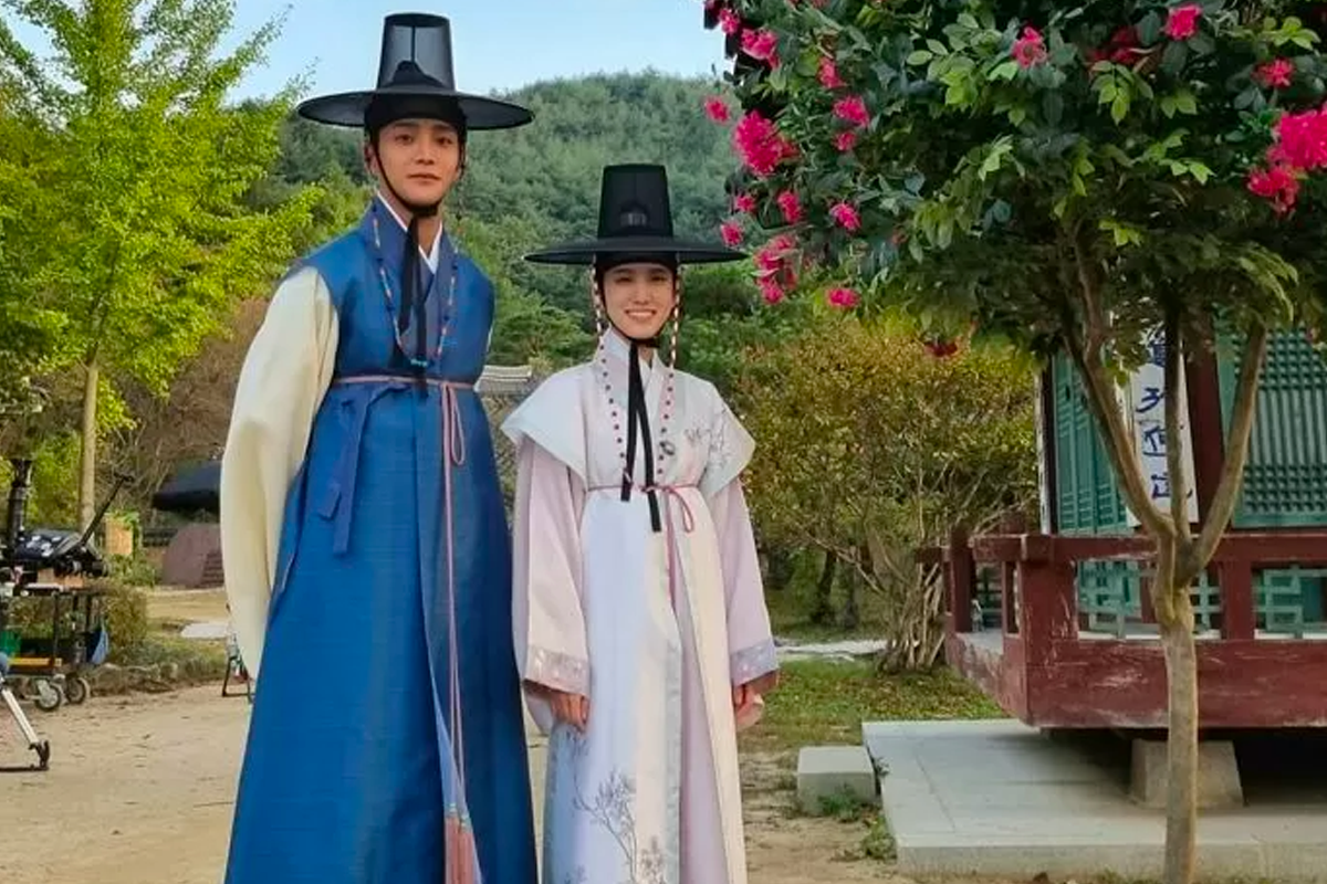 穿著韓服的兩人站在傳統韓國建築前，樹木和花朵環繞。