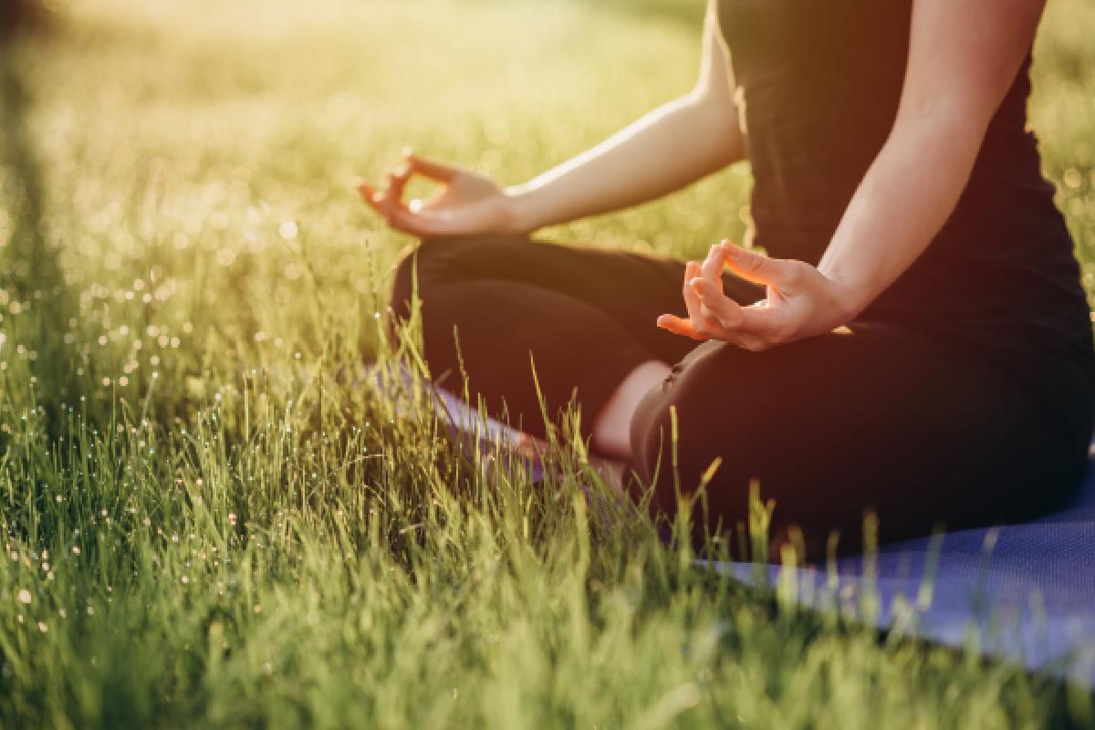 Personne méditant sur un tapis de yoga sur l'herbe, entourée par la nature, symbolisant la paix intérieure et la détente.