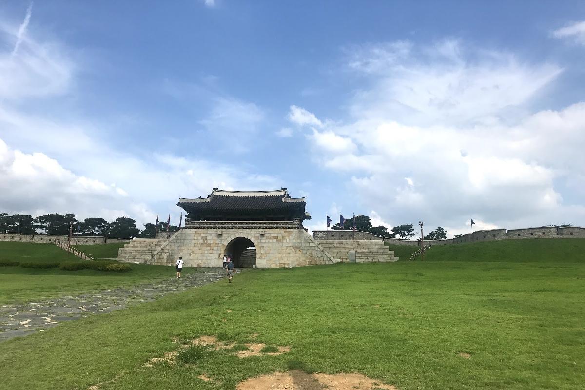 A picturesque view of Suwon Hwaseong Fortress, showcasing its historic architecture and vast green landscape under a blue sky.