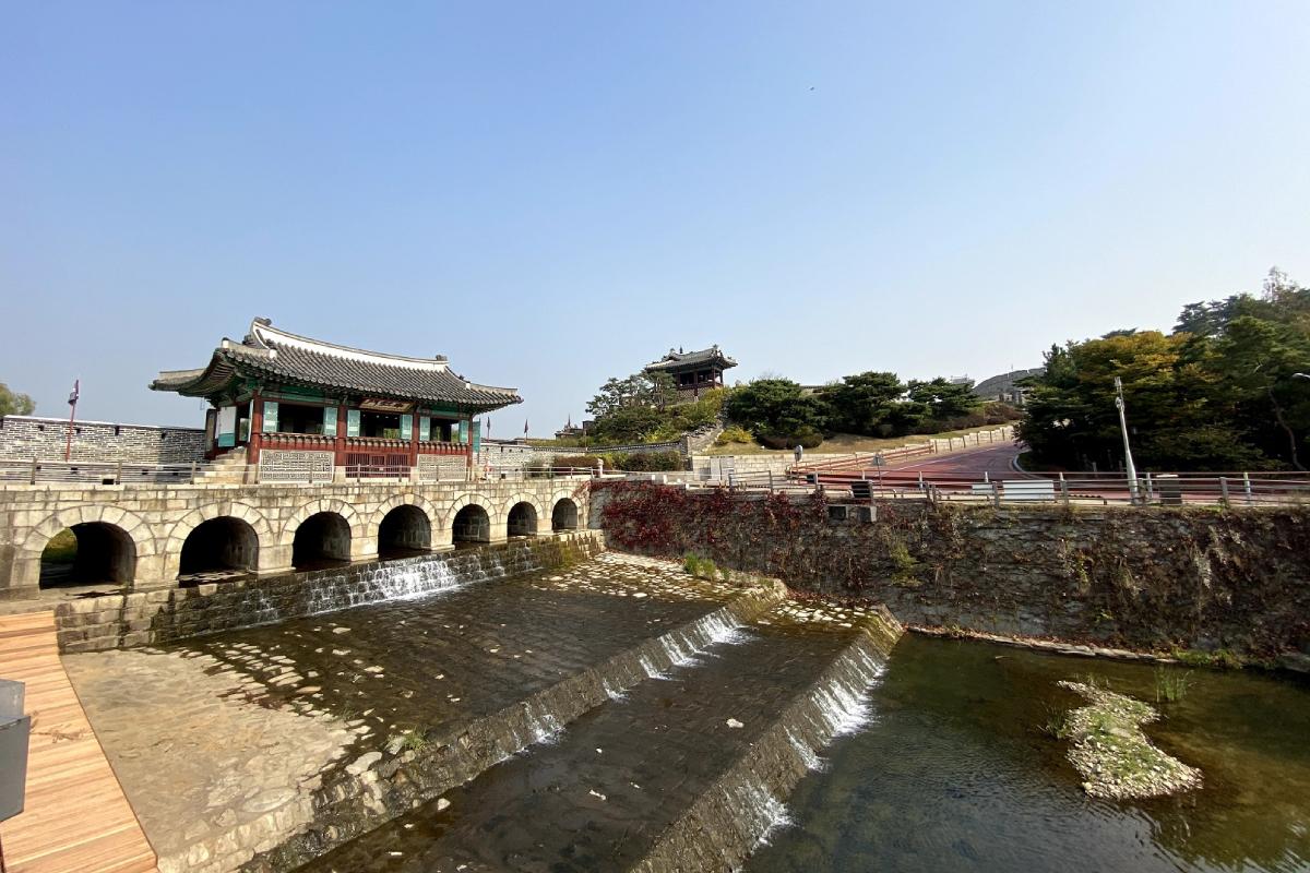 The serene beauty of the Hwaseong Fortress waterway, with traditional Korean pavilion architecture surrounded by lush greenery.