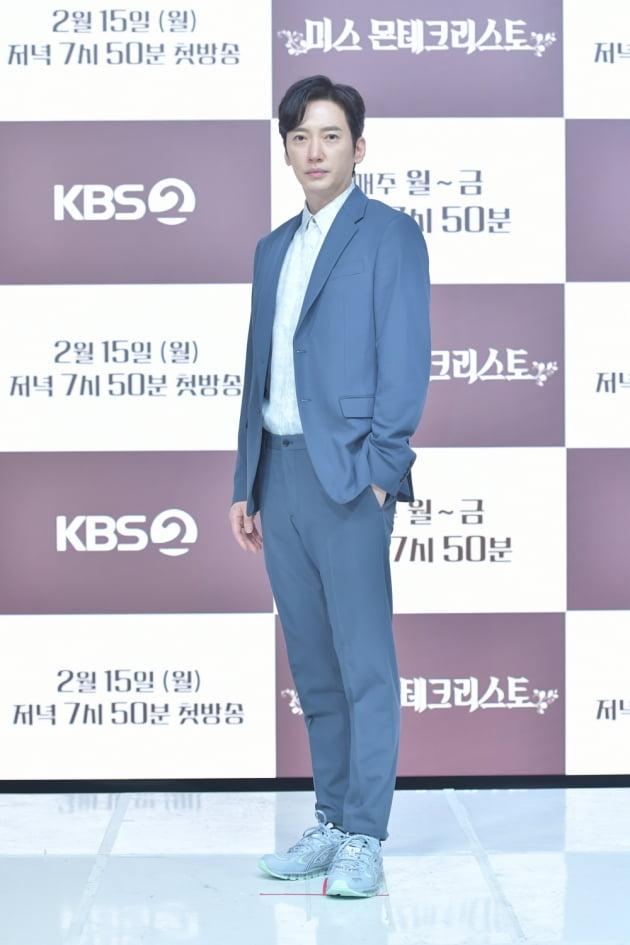 KBS2番組の記者会見で青いスーツを着た俳優、背景には『ミス・モンテ・クリスト』のプロモーションディスプレイがある。