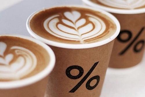 パーセントアラビカの美しいラテアートが施されたカフェラテ3つ。紙コップに描かれた%ロゴ。