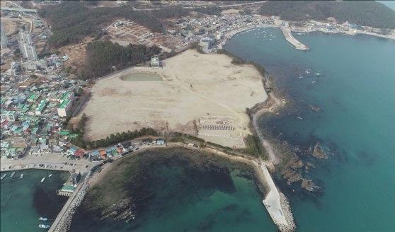 釜山市機張郡の旧韓国ガラス工場用地の空撮写真、釜山国際博覧会BTSコンサートの予定地として検討された場所、副題：海岸線と周囲のインフラ不足が問題視