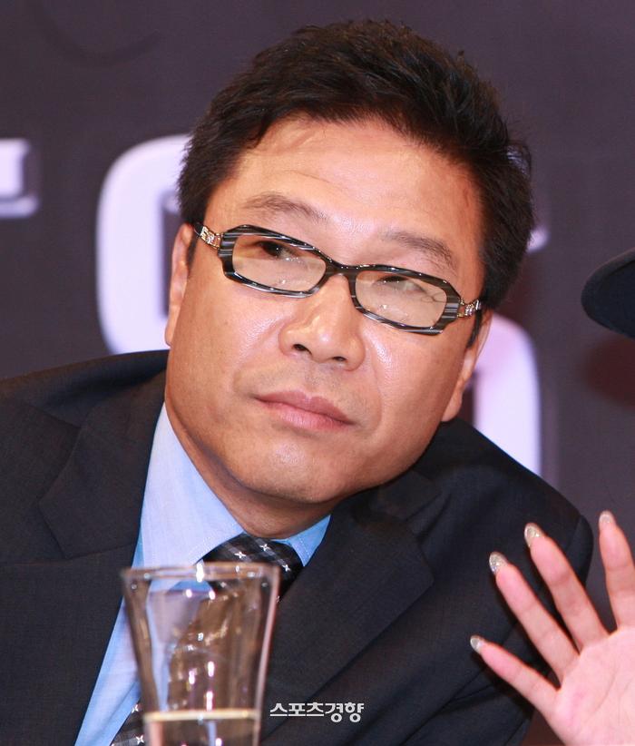 スーツ姿でガラスの水差しの前に座る人物