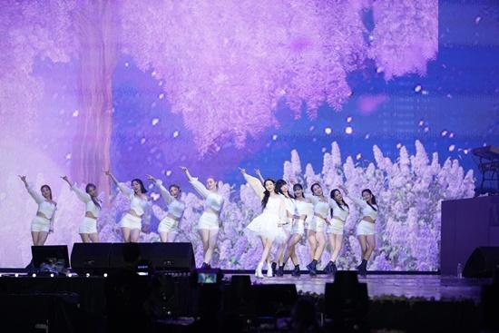 IUが鮮やかな背景のステージでバックダンサーを引き連れてパフォーマンスを行っている瞬間。躍動的なステージ演出が際立っている。