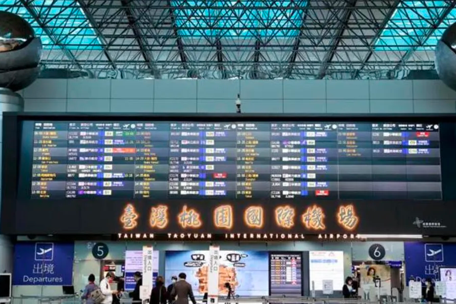 台湾桃园国际机场大厅显示屏上展示航班信息，入境和出境乘客在机场运作中，反映因疫情政策调整而逐渐复苏的旅游行业活动。