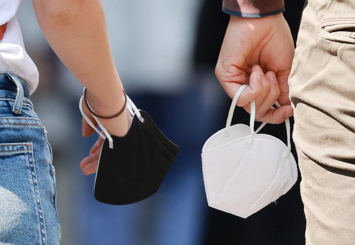 韓国のマスク着用規制が解除され、手に持たれる白と黒のマスク｜韓国の野外マスク義務解除のニュース