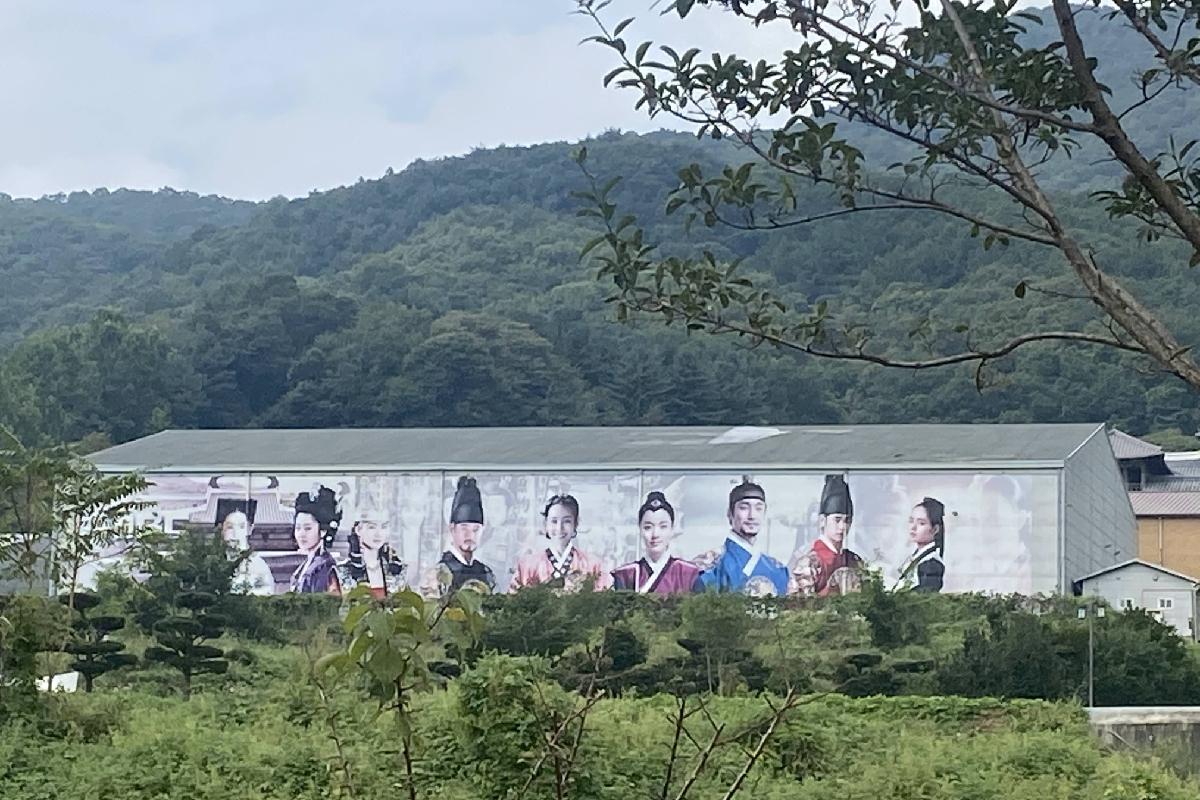 Panorama des paysages naturels et du grand bâtiment promotionnel au parc MBC Daejanggeum, avec des personnages costumés de dramas coréens.