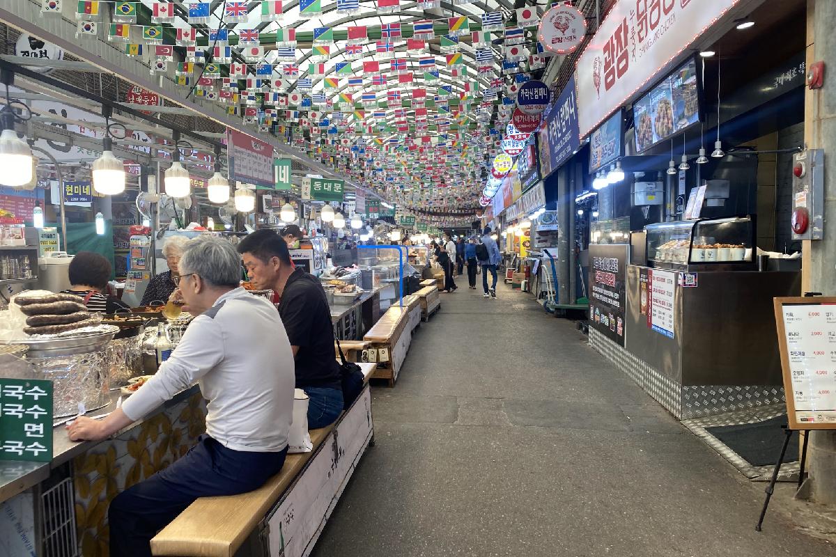 Intérieur du marché Gwangjang à Séoul, avec divers stands de nourriture de rue et des drapeaux internationaux accrochés au plafond
