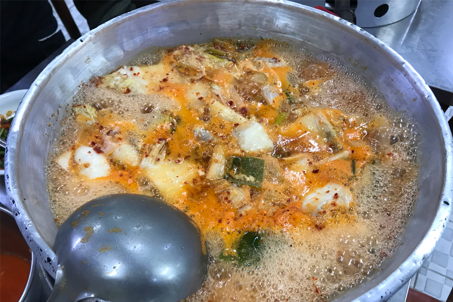 這是位於東大門的明洞一隻雞餐廳內，在煮著的紅色滾鍋雞湯，湯裡漂浮著泡菜、洋蔥等食材，散發著美味的香氣。