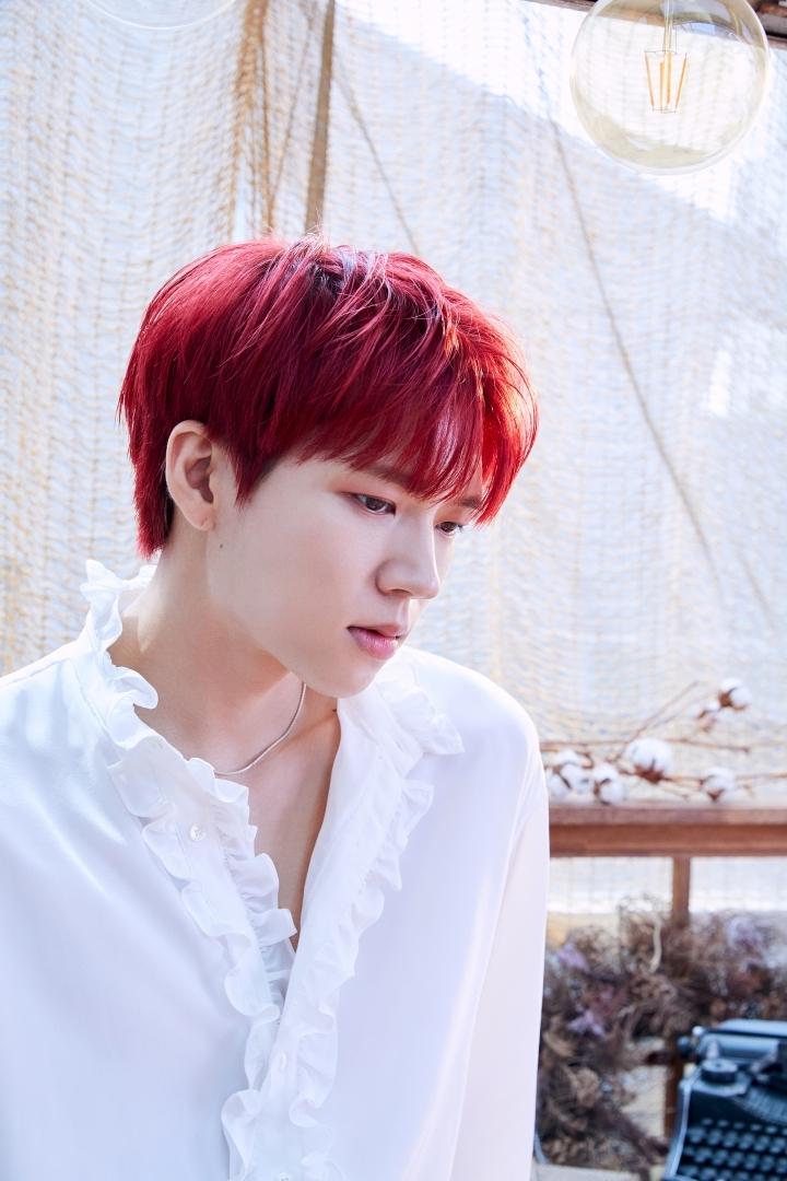 赤い髪のウヒョン、INFINITEのメンバーが白いシャツを着て室内のインテリアの前に立っている