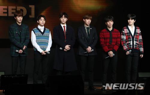 グループINFINITEの6人のメンバーがステージ上でフォーマルな服を着て立っている