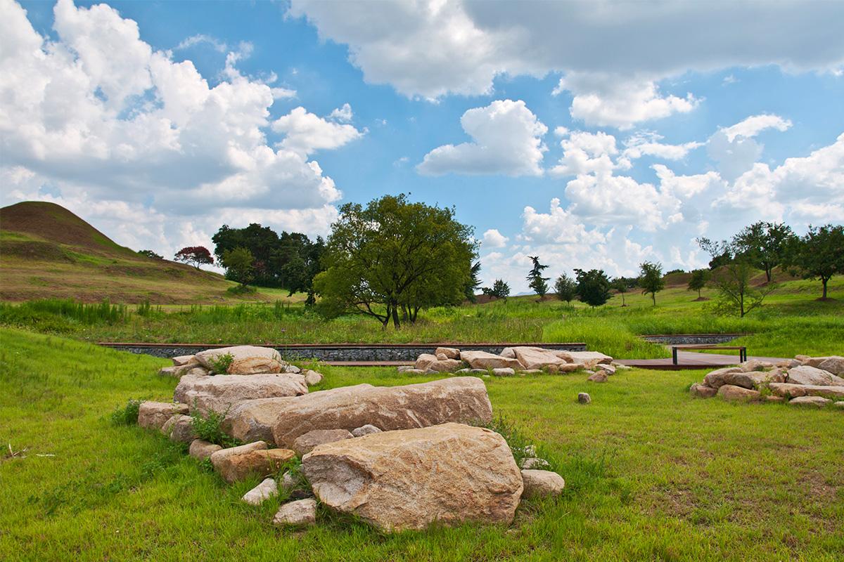 不老洞古坟群景观，展示了古墓群及周围环境，背景是蓝天和树木。