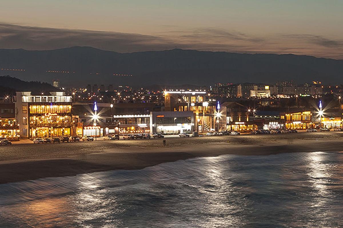 Calle de cafés en Playa Anmok iluminada por la noche, un lugar para disfrutar de una experiencia vibrante y relajante.