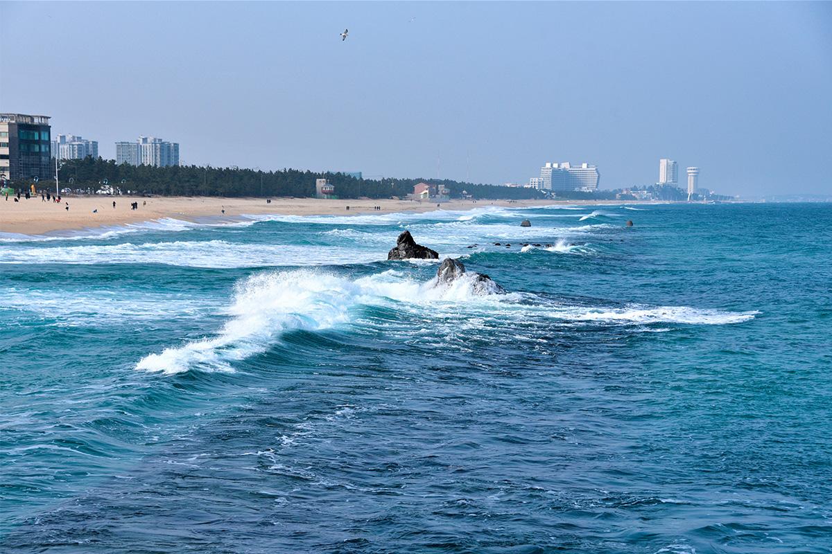 Vista de la Playa Anmok desde el agua, incluyendo olas y la costa de Gangneung.