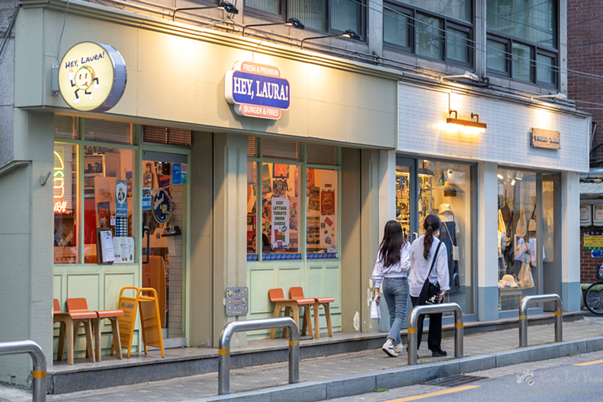 首尔麻浦区望理团路的一家色彩鲜亮的餐厅，门前有两个年轻女性正在行走。