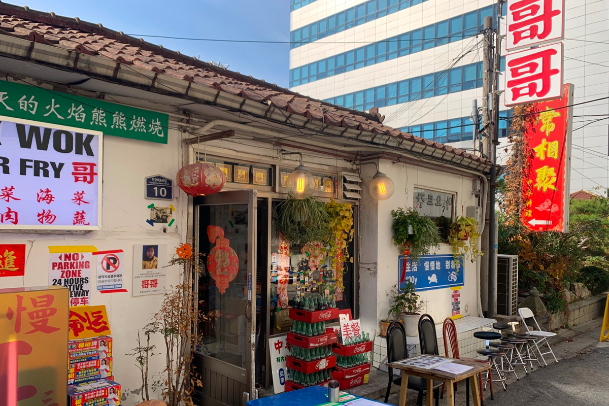 位于新龙山的龙理团路，图中是上世纪风格的中餐馆，配有中文招牌和广告。