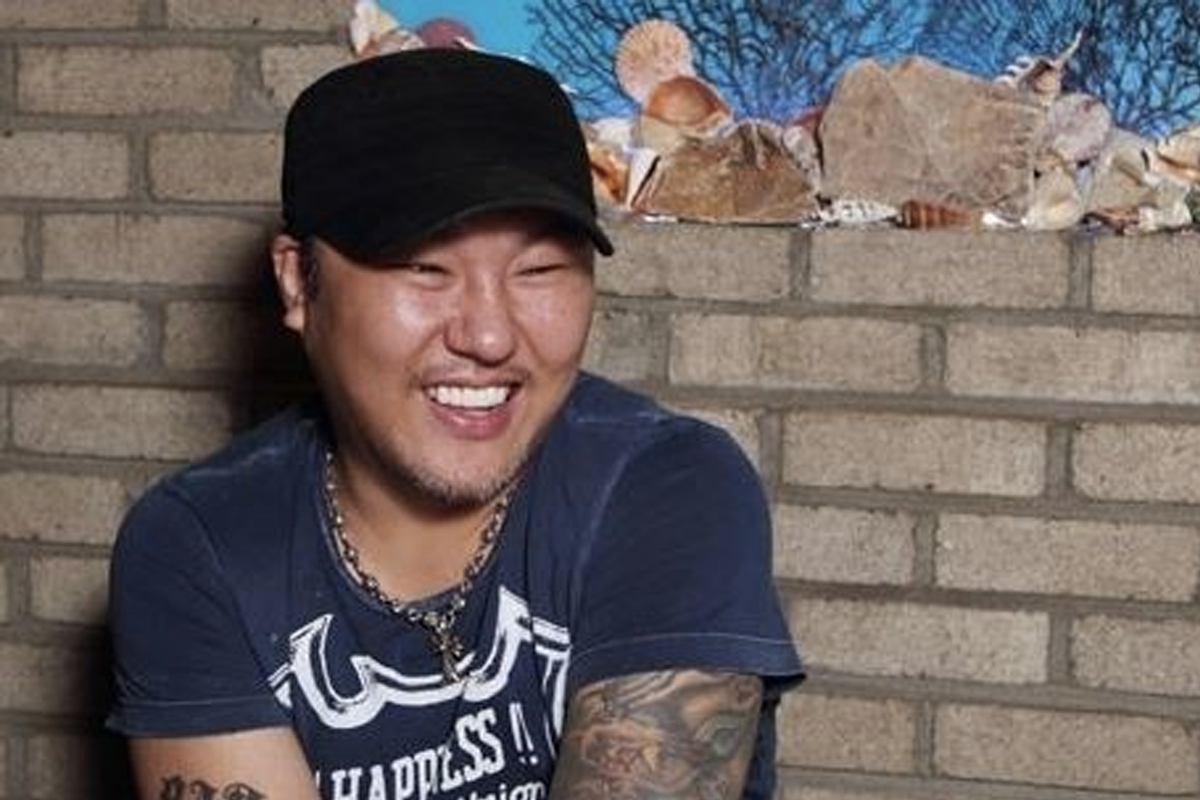 纹身的男子穿着帽子和深色T恤，坐在砖墙前。