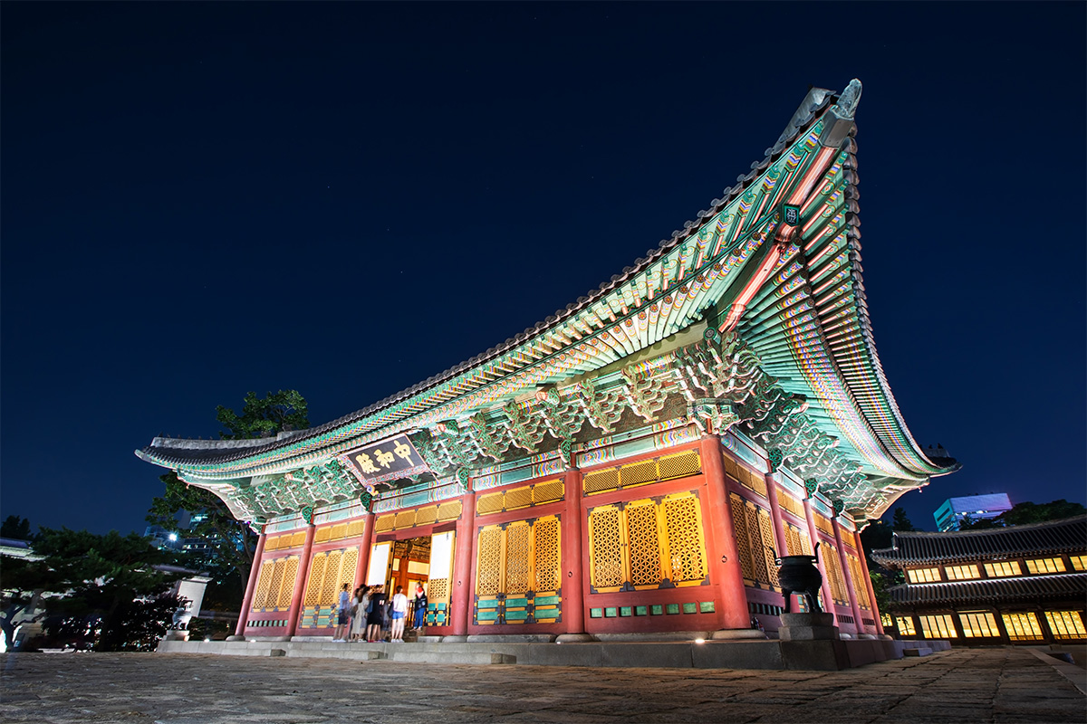 Junghwajeon, sảnh chính của Cung điện Deoksugung vào buổi tối, tỏa sáng dưới ánh đèn với bầu trời đêm làm nổi bật sự lộng lẫy của các chi tiết kiến trúc gỗ và ngói