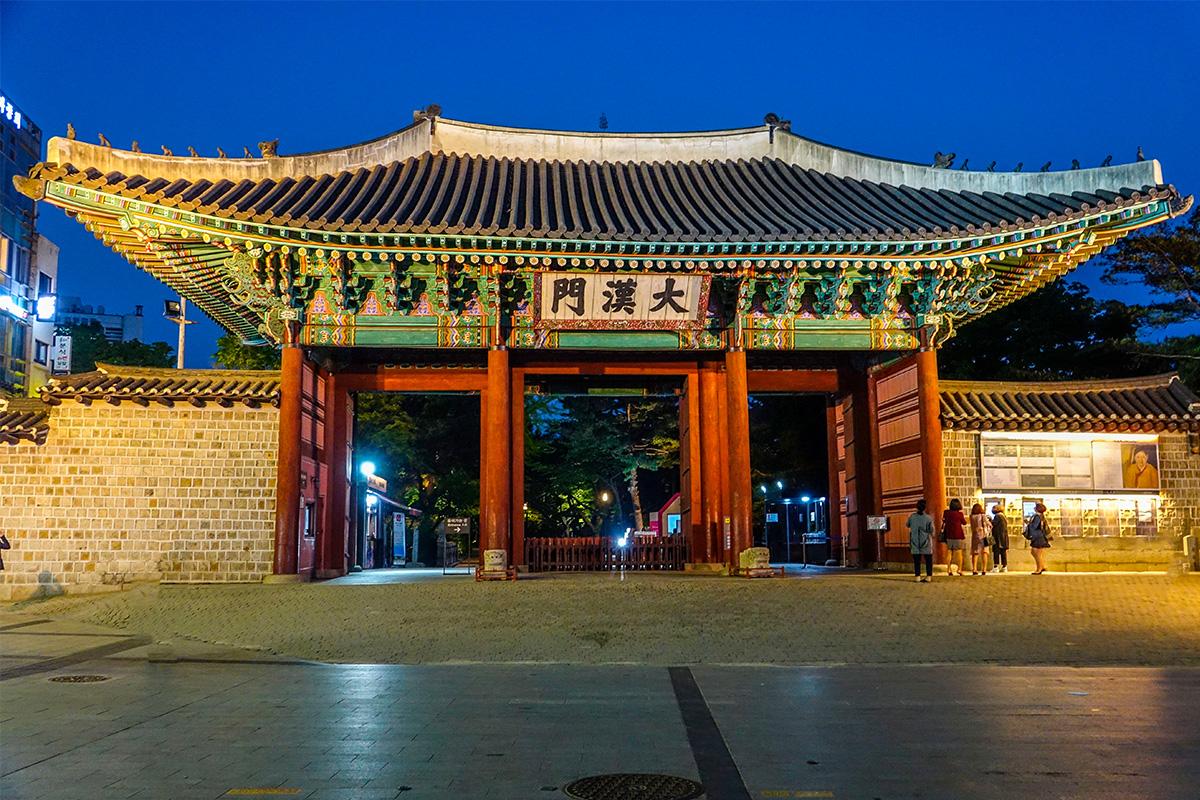 Daehanmun, la porte d'entrée du Palais Deoksugung, illuminée et entourée de lumières nocturnes.