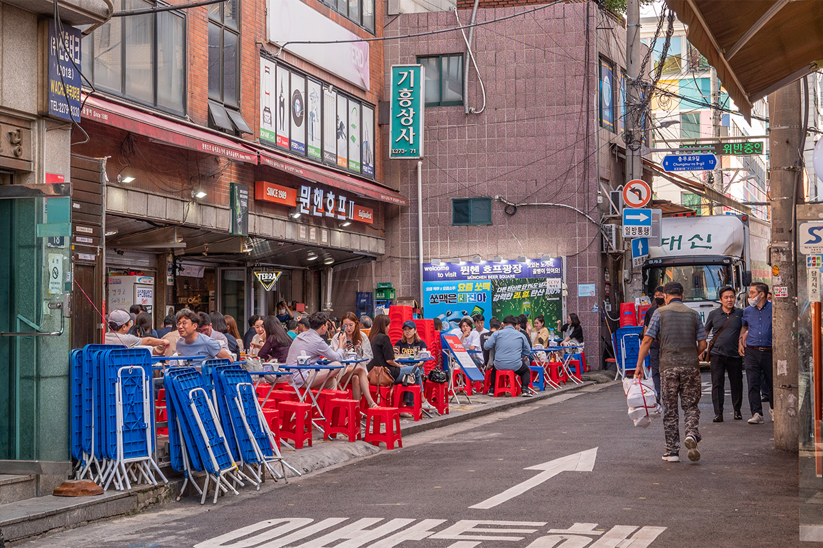 Mesas al aire libre en un restaurante de Euljiro, Seúl, con comensales disfrutando de comida y bebida en un ambiente urbano.