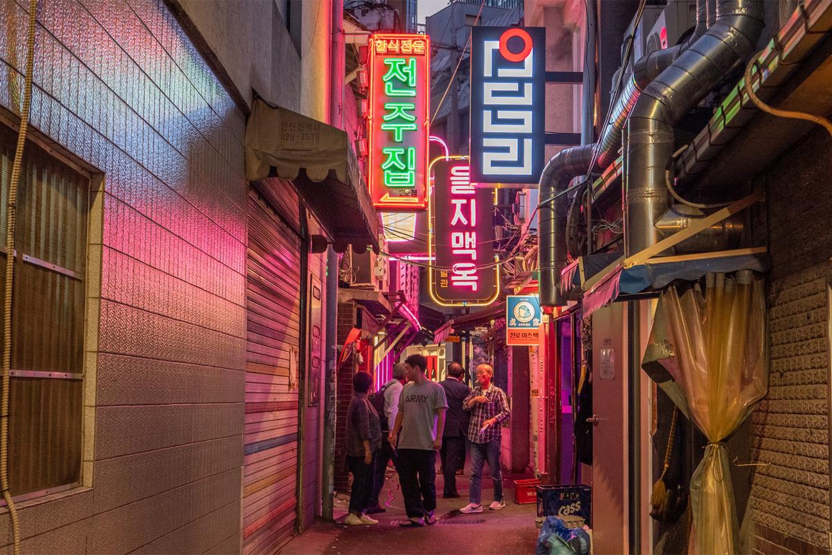 Callejón iluminado con luces de neón en Euljiro, Seúl, mostrando una mezcla de letreros antiguos y modernos.