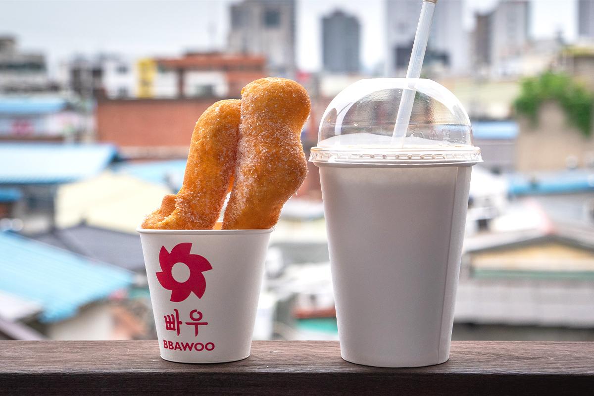 Delicia coreana tradicional en un vaso de papel junto a una bebida, con el horizonte de Seúl como fondo.