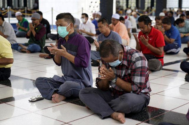 一群穆斯林男性信徒在马来西亚清真寺内坐在地上祈祷，展示宗教信仰对性别与性取向的法律影响。