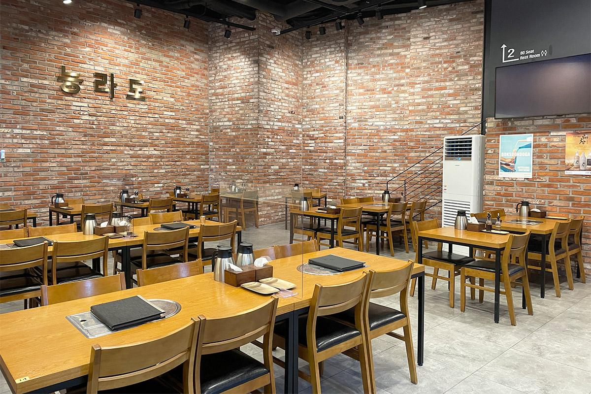 明洞绫罗岛餐馆内景，展示了餐桌和墙壁上的砖瓦设计，营造出温馨舒适的用餐环境。