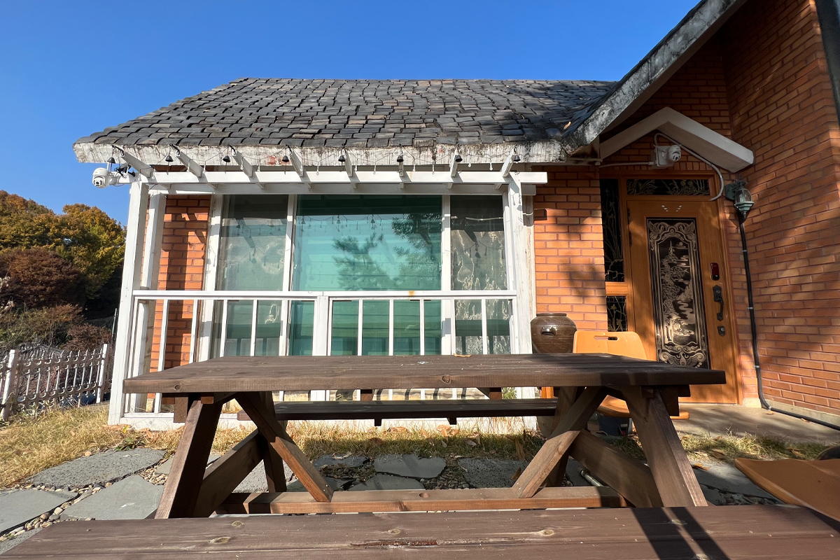 Cửa trước và sân nhỏ của ngôi nhà nhân vật Hee-Do từ Twenty-Five, Twenty-One với băng ghế ngoài trời