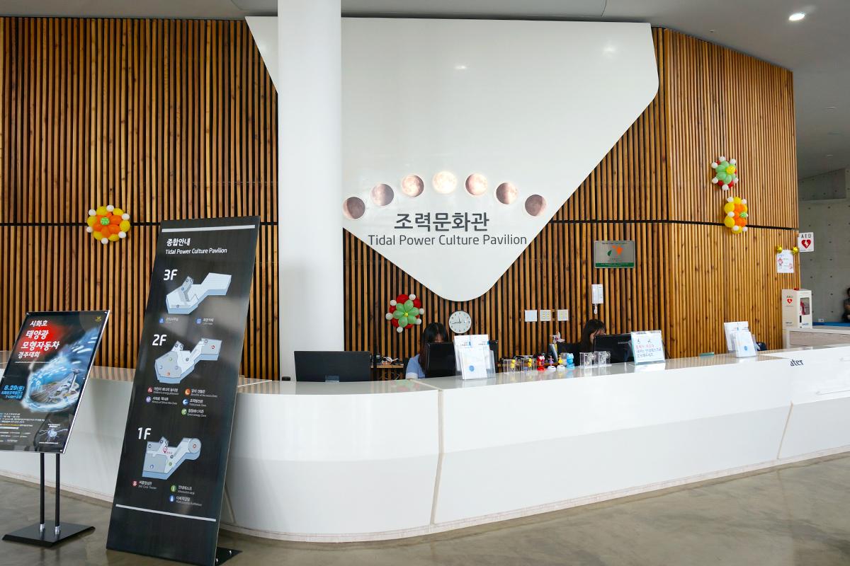 Reception area of Tidal Power Culture Pavilion at the Sihwa Lake Tidal Power Plant with a wooden panel design and information desk.