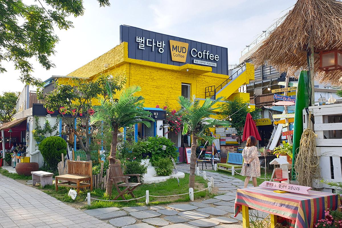 Exterior of MUD Coffee with colorful decorations and plants, creating a vibrant and inviting environment on Dangneomeo Beach.