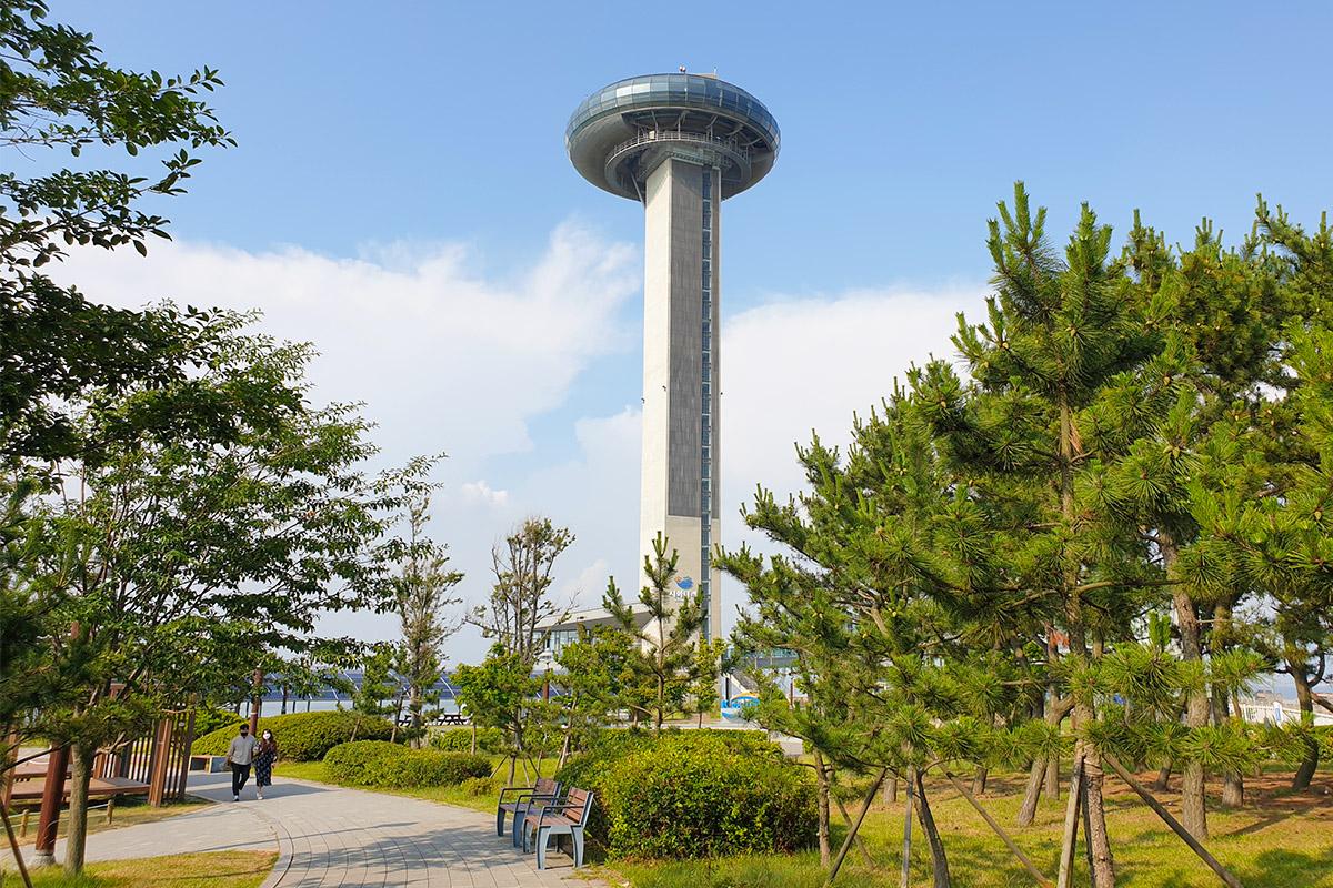 View of the Moon Observatory at the Sihwa Lake Tidal Power Plant in South Korea, surrounded by trees and featuring a scenic pathway.