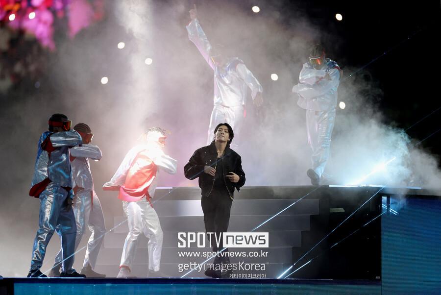 BTSのジョングクがカタールワールドカップのステージで先頭に立ち、共演者とともにパフォーマンスを行っているシーン。