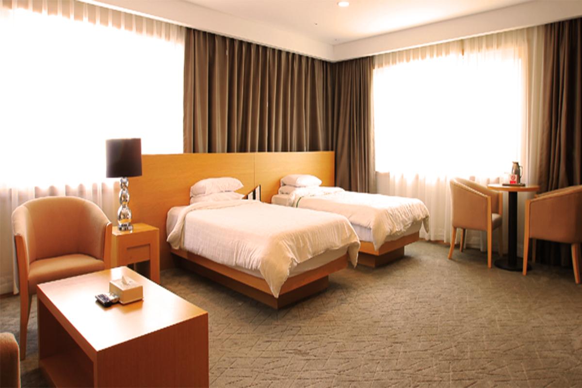 Interior of a hotel room at Dragon Valley Hotel with two single beds, chairs, and a table.
