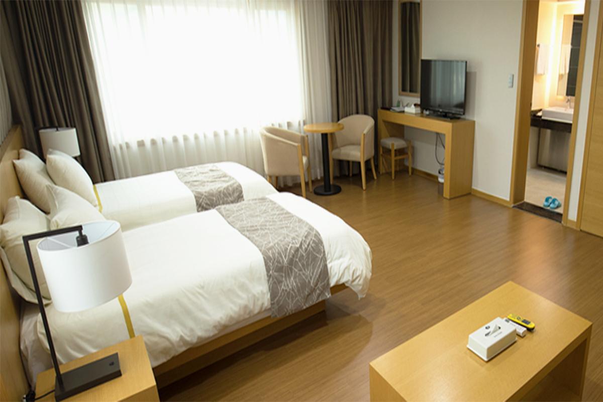 Spacious hotel room with two single beds, a large window, and a flat-screen TV.