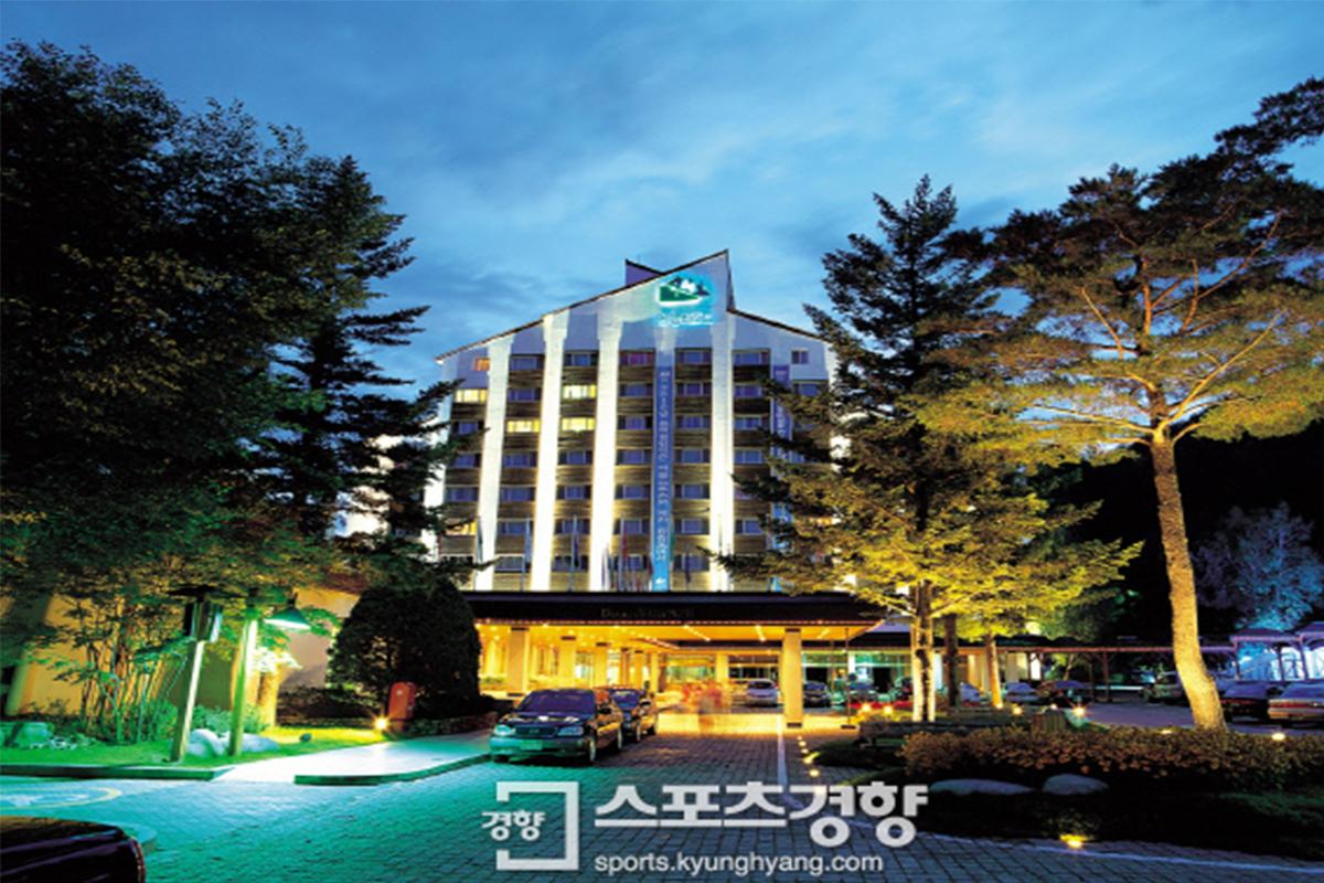 Exterior view of Dragon Valley Hotel lit up at night, surrounded by trees.