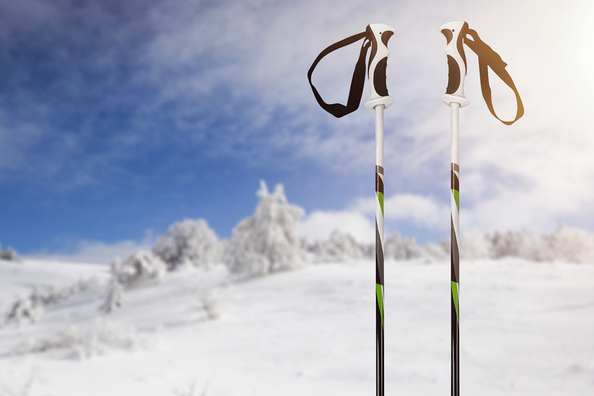 Ski poles standing in the snow with a snowy landscape and cloudy blue sky in the background.