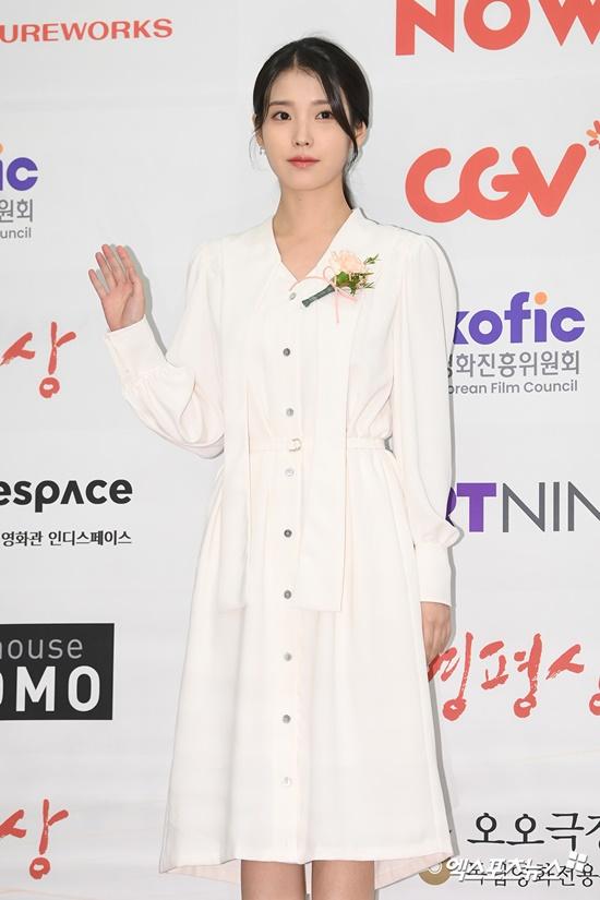 韓国映画評論家協会賞のイベントで白いドレスを着た人物がレッドカーペットに立ち、カメラに向かって手を振っている。背景には映画関連のスポンサーのロゴが見える。