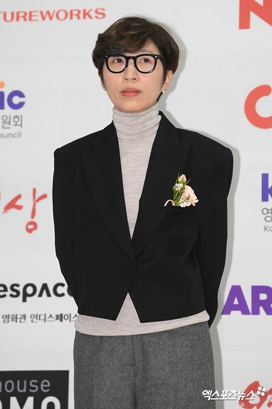 韓国映画評論家協会賞で黒いスーツを着た受賞者が素樸な花のコサージュを身につけ、地面に手を置いてポーズを取っている。背景にはイベントのロゴが記されている。