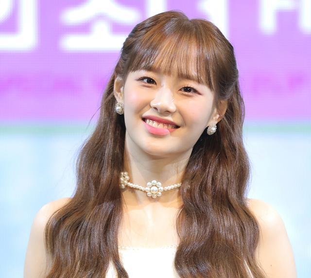 今月の少女のメンバー、明るい背景で撮影された女性の上半身。女性は長いウェーブのかかった髪で、パールのアクセサリーを身につけています。