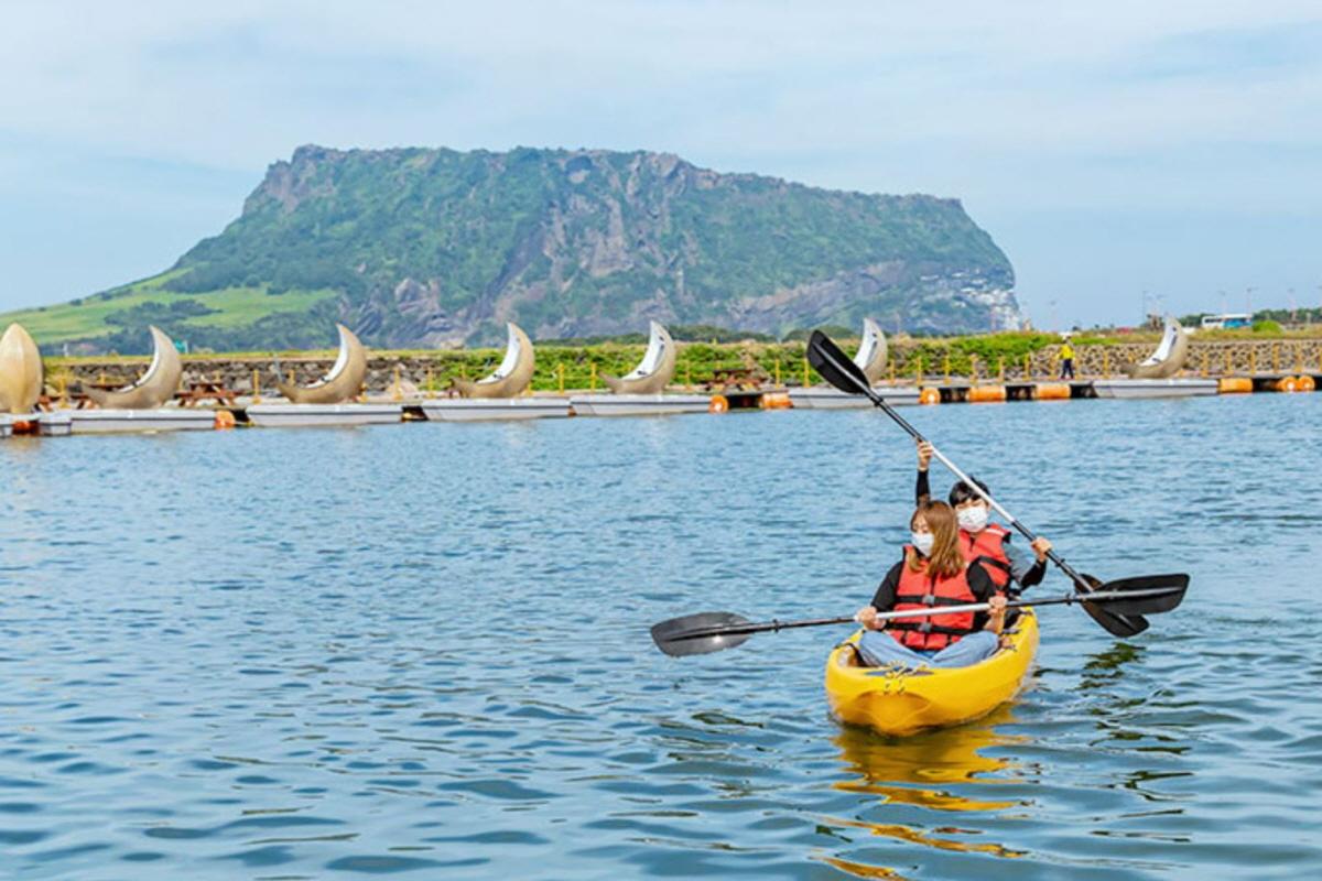 Deux personnes faisant du kayak sur l'eau avec des bateaux en forme de lune et le pic Seongsan Ilchulbong en arrière-plan sur l'île de Jeju, Corée du Sud.