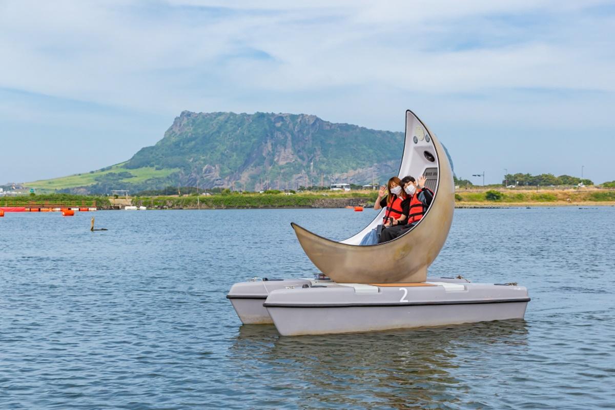 Photo d'un bateau en forme de lune flottant sur l'eau avec le pic Seongsan Ilchulbong en arrière-plan sur l'île de Jeju, Corée du Sud.