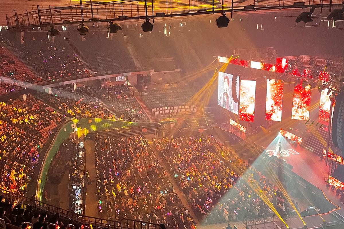 Крупный зал с участниками, смотрящими выступление на сцене с экранами и световыми эффектами