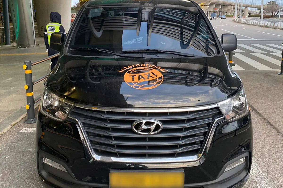 현대차의 국제 운송 택시가 공항 도로에 주차되어 있는 모습입니다. 국제 여행객을 위한 교통 수단을 홍보하는 이미지로 적합합니다.