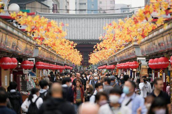 東京浅草の賑やかな通り、紅葉の装飾が施された両側に多数の人々が歩いている。訪日観光客の増加を表す光景。