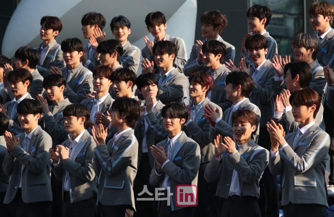 Mnet『BOYS PLANET』の参加者たちが上巌洞DMC文化公園で一斉にスタンディングオベーションを行っています。彼らの意気込みと結束を示す場面です。多くの人々が見守る中、参加者たちがデビューへの意欲を表しています。