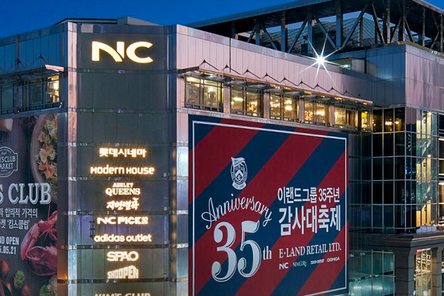 Visit Busan 推介，绿色树木背景下的NC百货，舒适的购物氛围，适合家庭和个人的理想购物目的地。