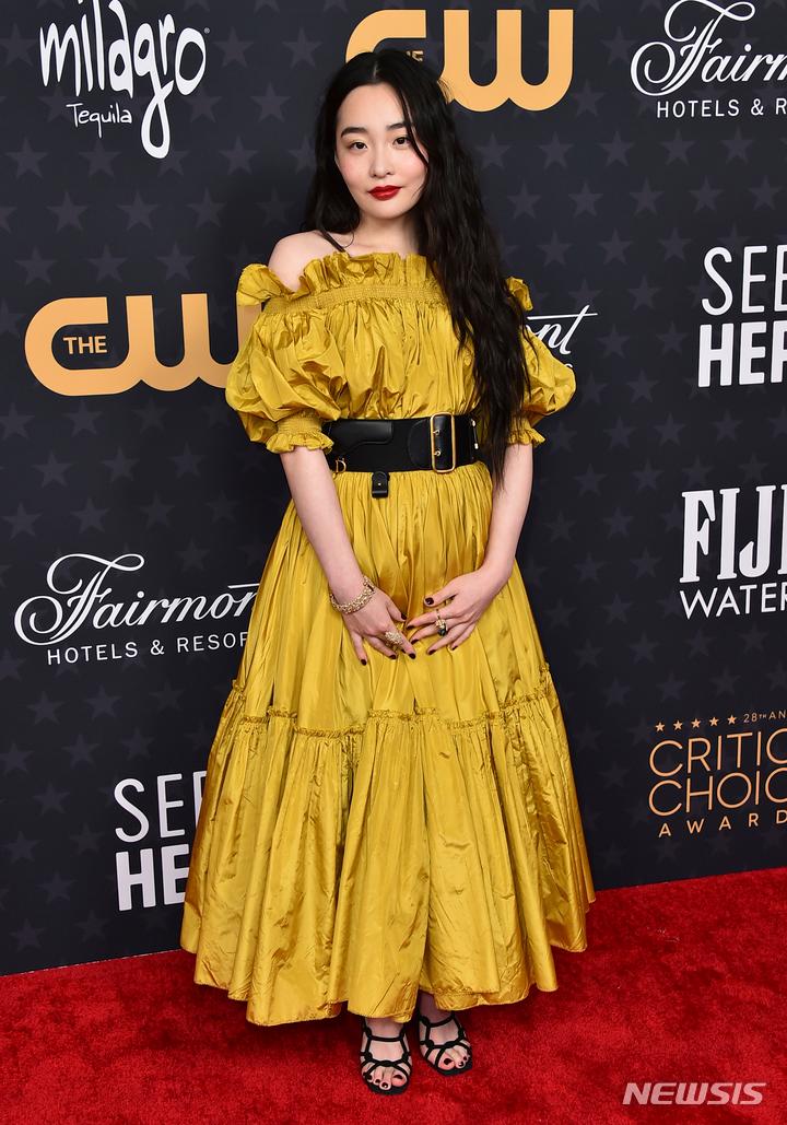 黄色のドレスを着た女性、アワードセレモニー出席、赤いカーペットの上に立つ、左手でドレスのすそを持つ